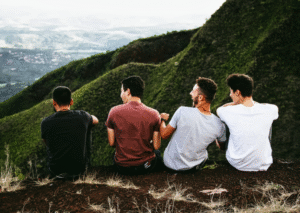 Vier Männer sitzen auf Berghang und blicken auf Berglandschaft, Rückenansicht